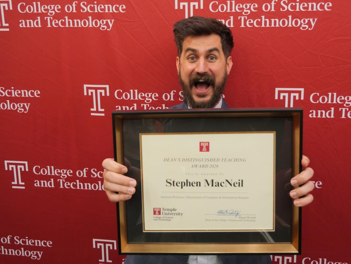 Stephen MacNeil smiling and holding the Dean's Distinguished Teaching Award plaque in front of a Temple CST backdrop.