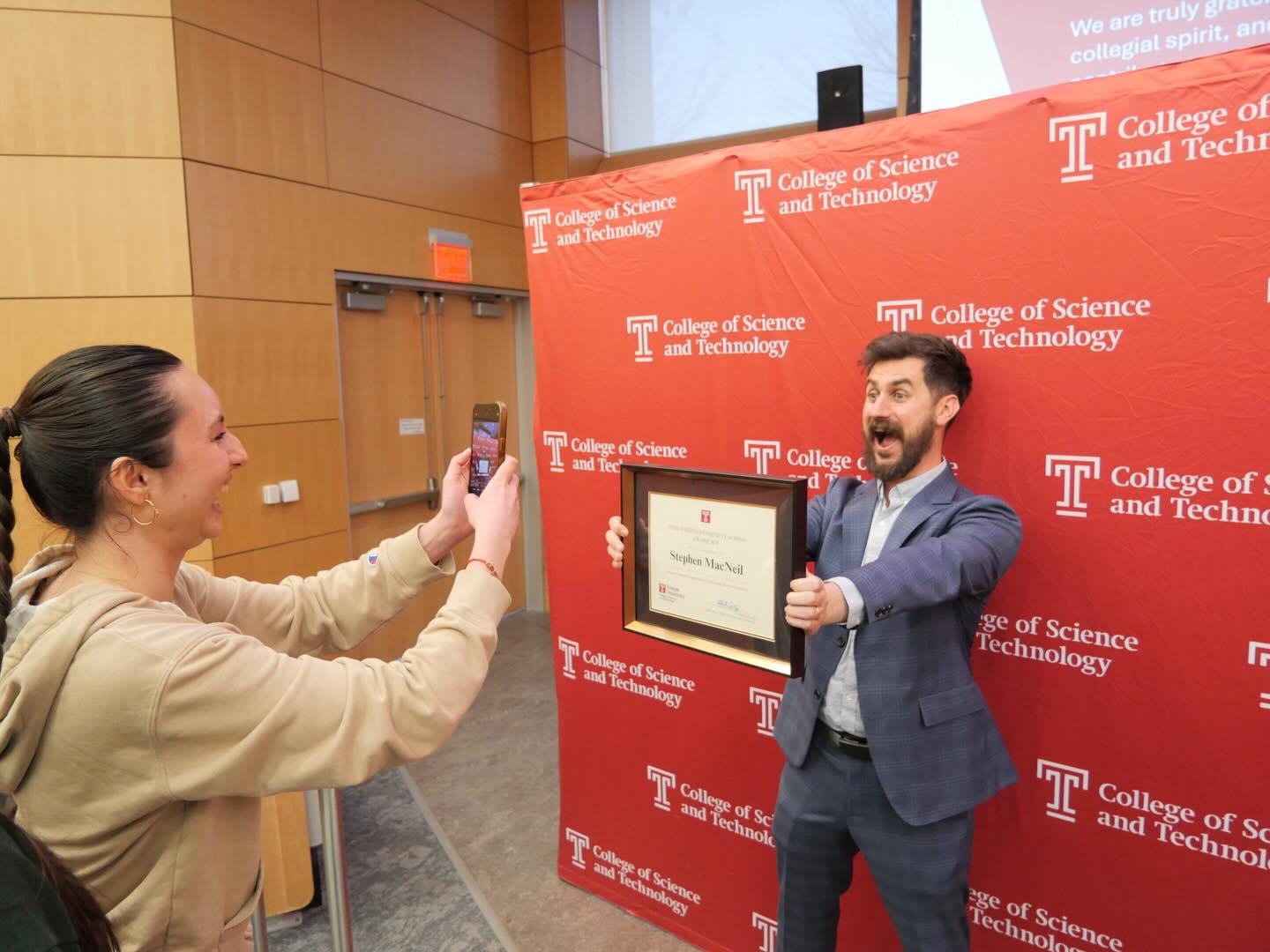 Stephen MacNeil holding the award while students take photos during the event.